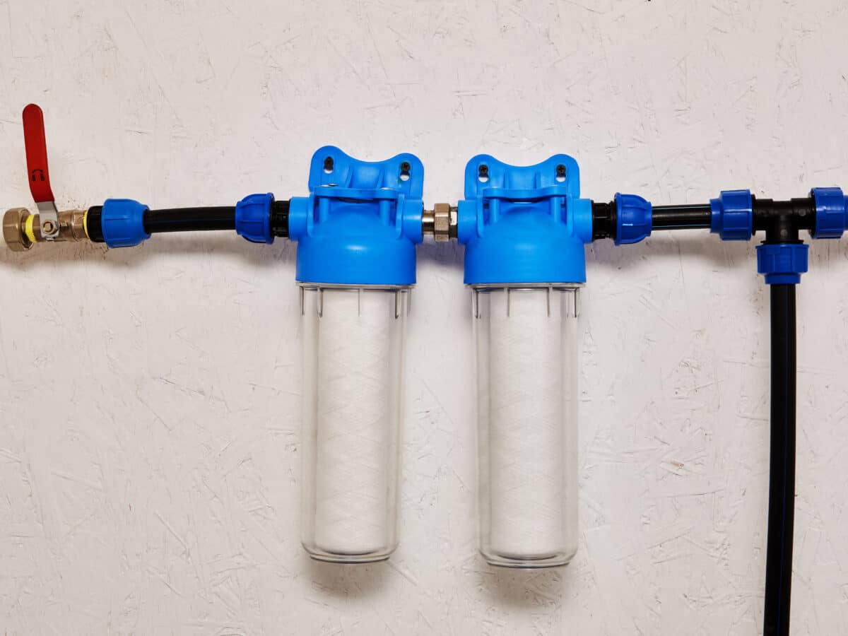 Close-up of inline water filter housings mounted on a water supply line, used to filter sediment before it reaches the system