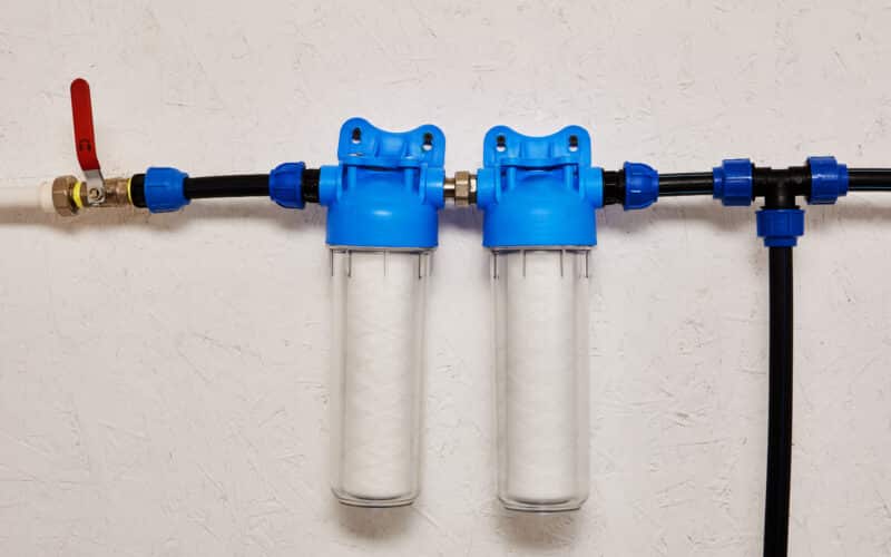 Close-up of inline water filter housings mounted on a water supply line, used to filter sediment before it reaches the system