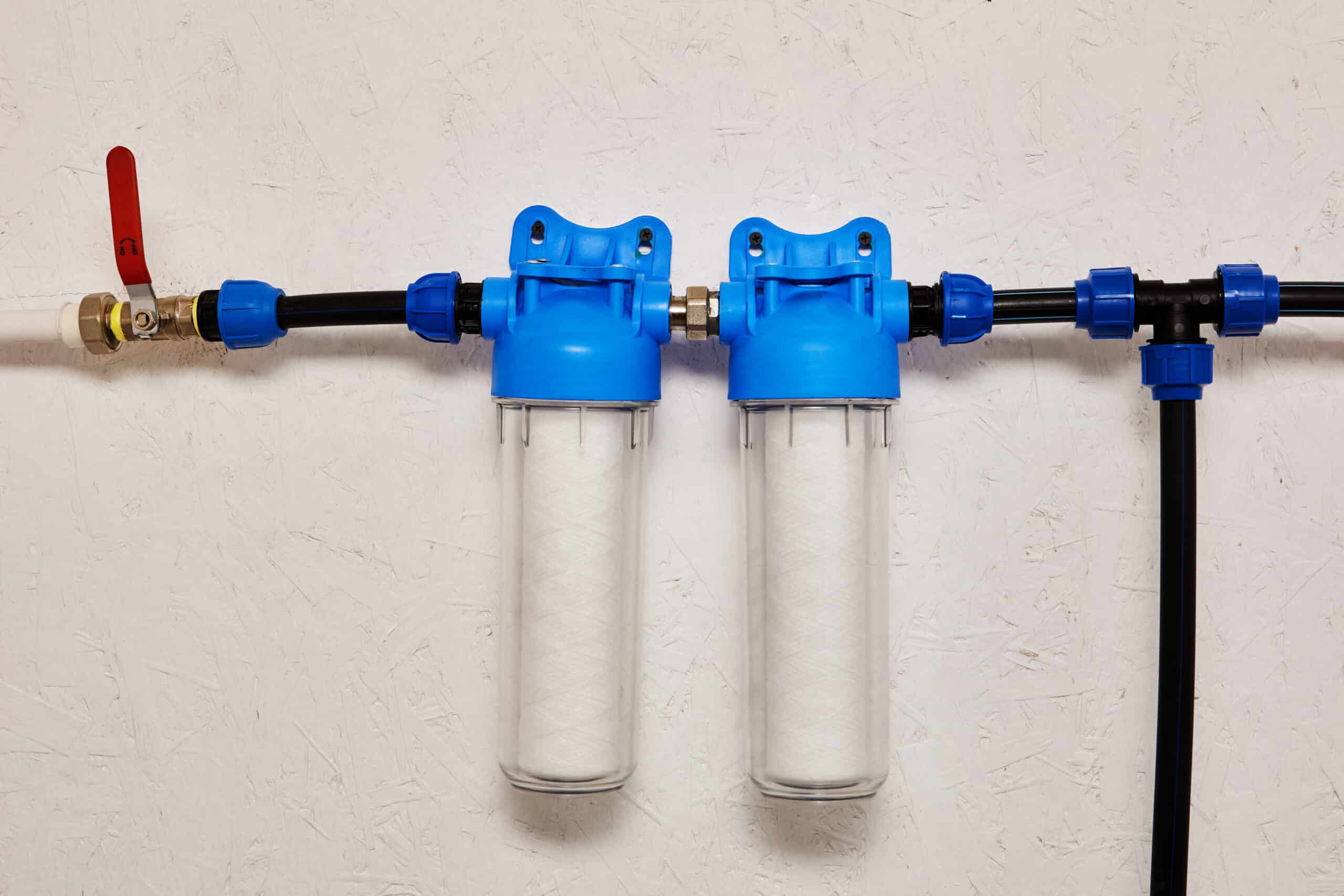 Close-up of inline water filter housings mounted on a water supply line, used to filter sediment before it reaches the system