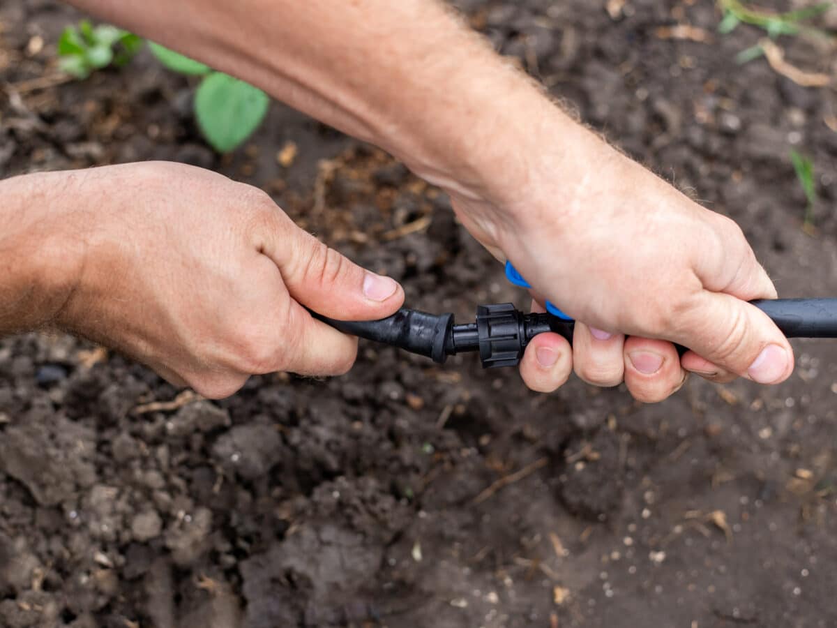 Coiled black polyethylene tubing, fittings, and a punch tool laid out on grass for a DIY drip irrigation system