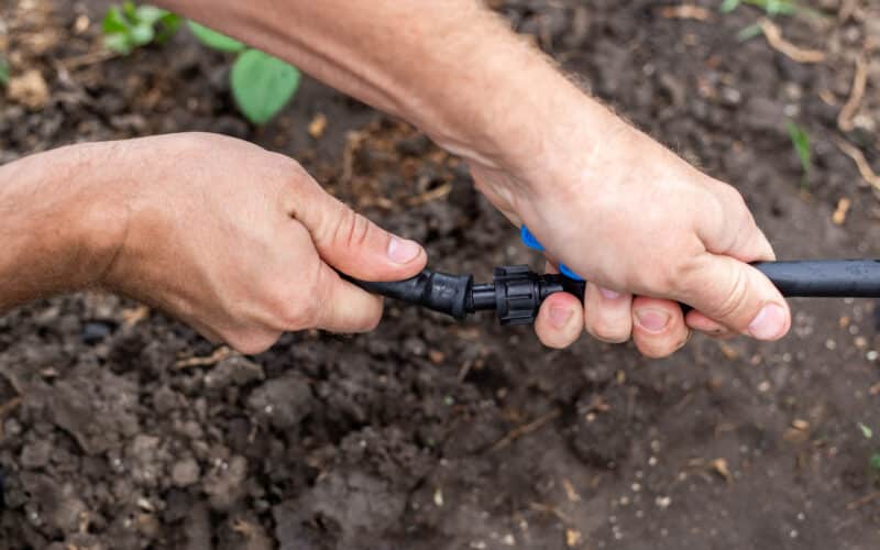 Coiled black polyethylene tubing, fittings, and a punch tool laid out on grass for a DIY drip irrigation system