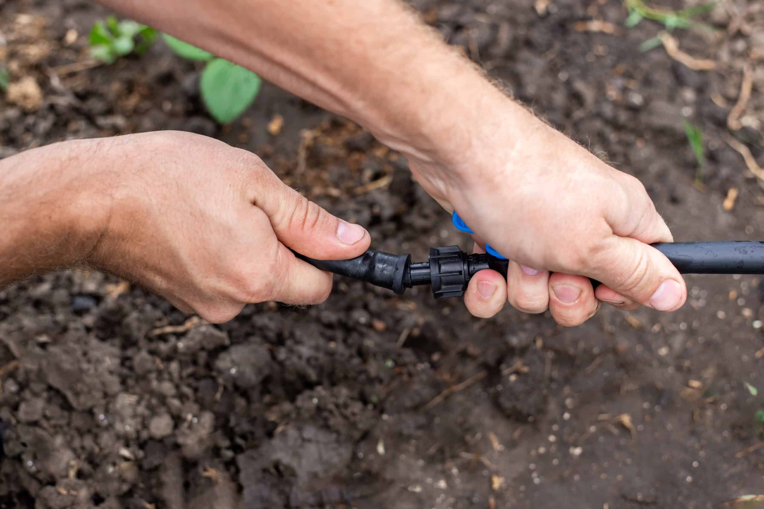 Coiled black polyethylene tubing, fittings, and a punch tool laid out on grass for a DIY drip irrigation system