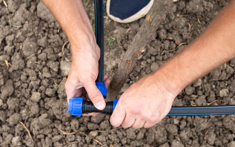 A gardener installing a drip irrigation system kit by connecting HDPE tubing fittings