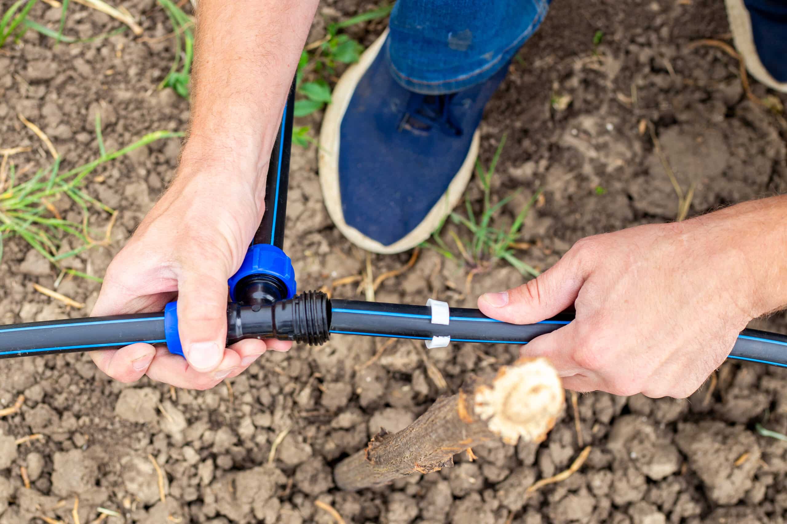 Hands punching a barbed connector into half-inch drip tubing for a raised bed system
