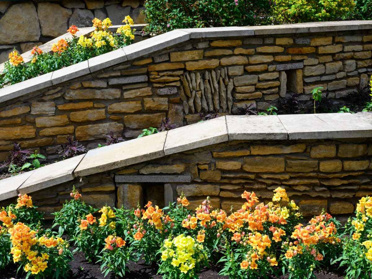 Terraced stone retaining walls holding a sloped backyard flower bed, the kind of layout where drip irrigation needs pressure-compensating emitters to water evenly top to bottom