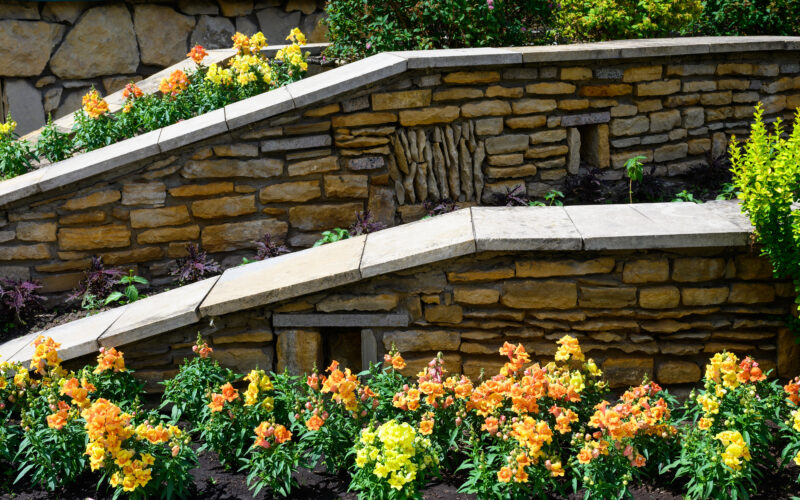 Terraced stone retaining walls holding a sloped backyard flower bed, the kind of layout where drip irrigation needs pressure-compensating emitters to water evenly top to bottom
